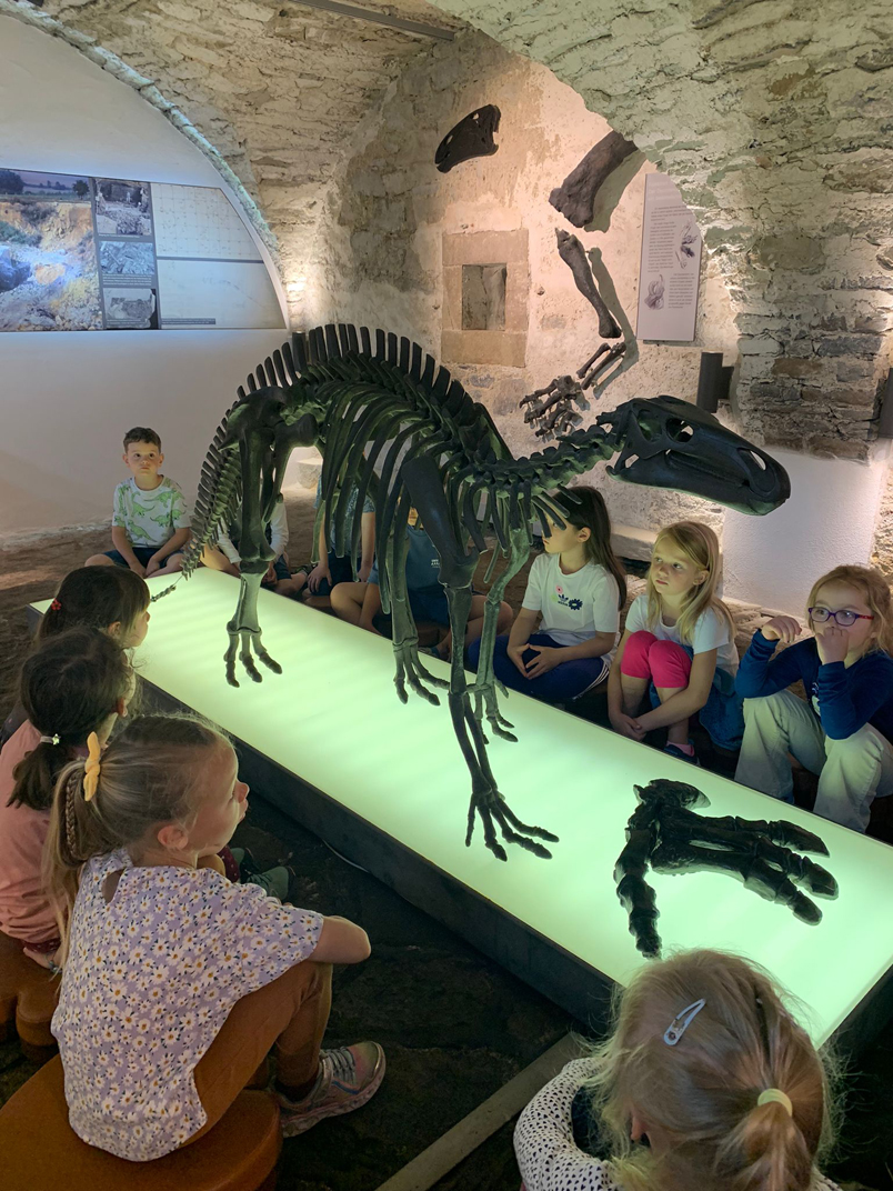 Kinder betrachten in einem Kellergewölbe das Skelett eines Dinosauriers