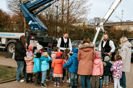 Handwerker und Kinder vor einem großen Kran
