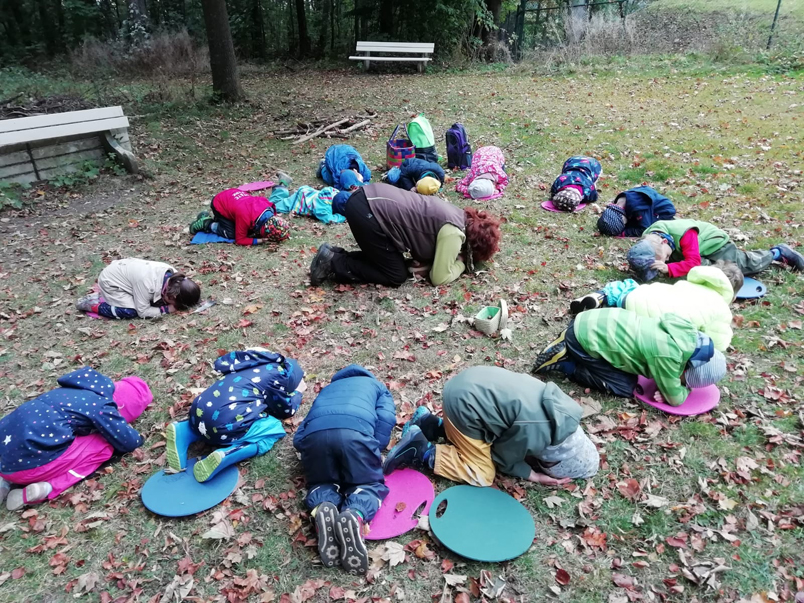 Kinder hocken im Kreis auf dem Waldboden