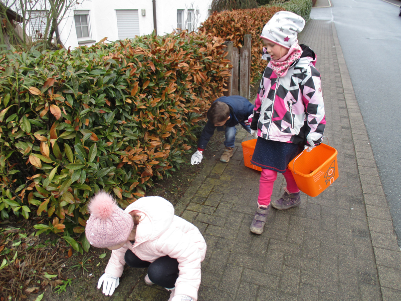 Kinder suchen Müll in einer Hecke
